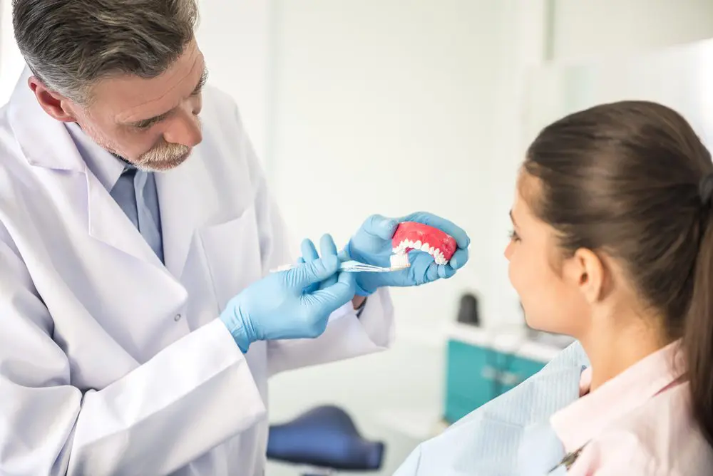 Cheerful dentist teaching on model of human teeth how right to brush teeth his female patient.