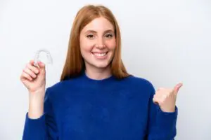 Young redhead woman holding invisible braces - Smilebliss