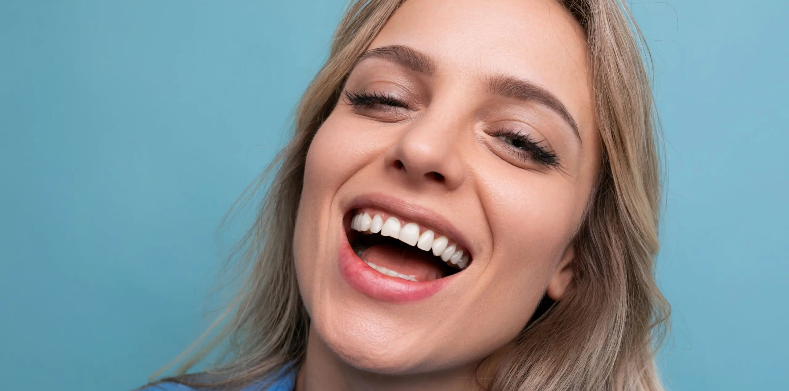 stylish casual blonde girl flirts and smiles on a blue isolated background