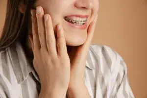 young woman with braces hold cheeks with her hands on beige background