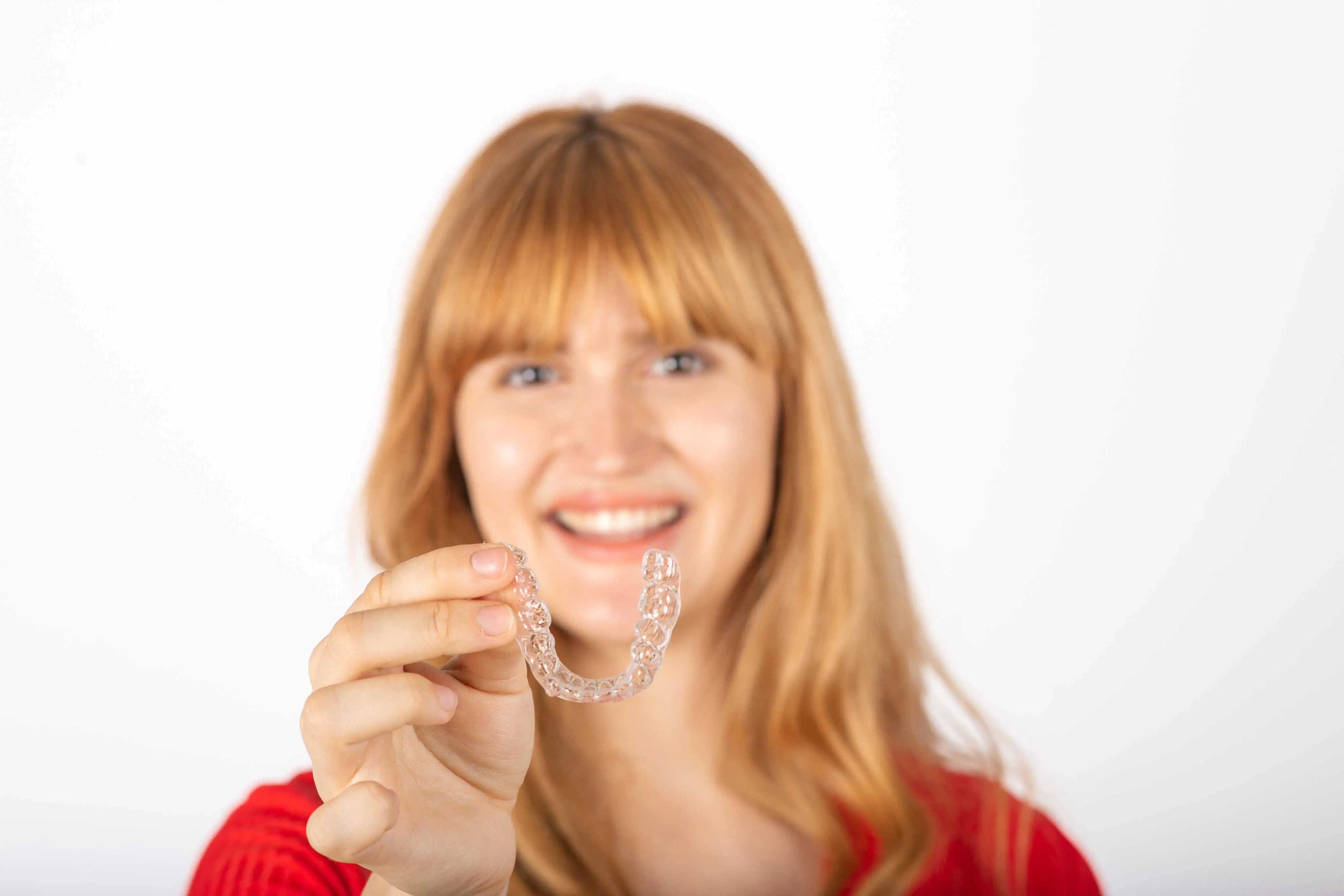 young woman smiling while holding clear aligners