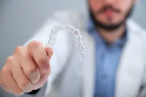 Unrecognizable young orthodontist holding invisible dental aligners.