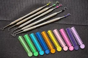 Colorful orthodontic ligatures and stainless steel instruments for procedure of attaching braces to teeth. Black napkin with orthodontic tools and multicolored rubber bands for braces.