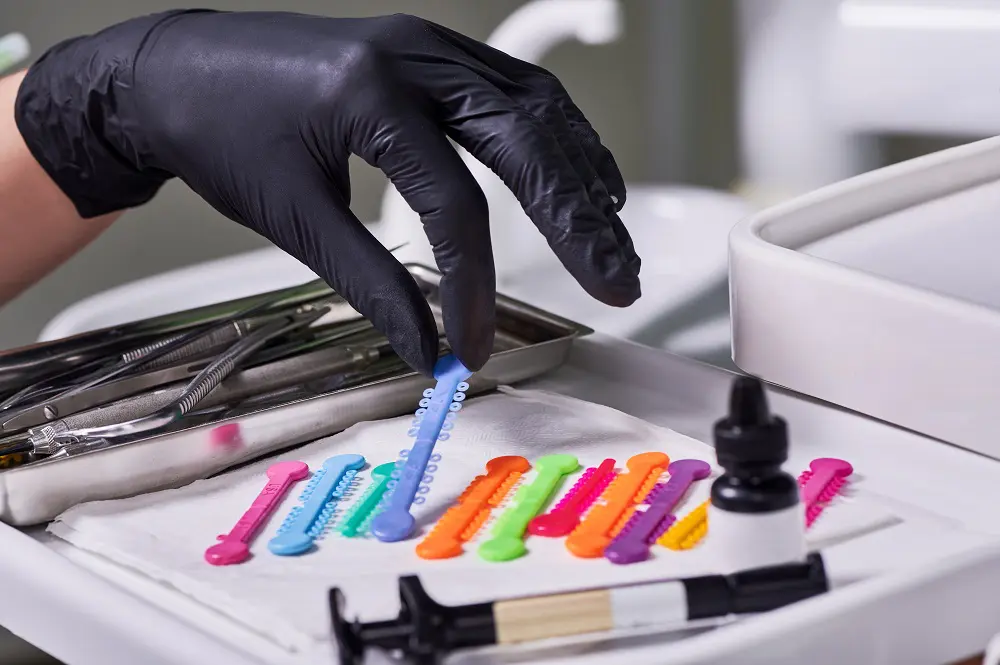 Close up of doctor hand in sterile glove grabbing blue orthodontic ligature tie.