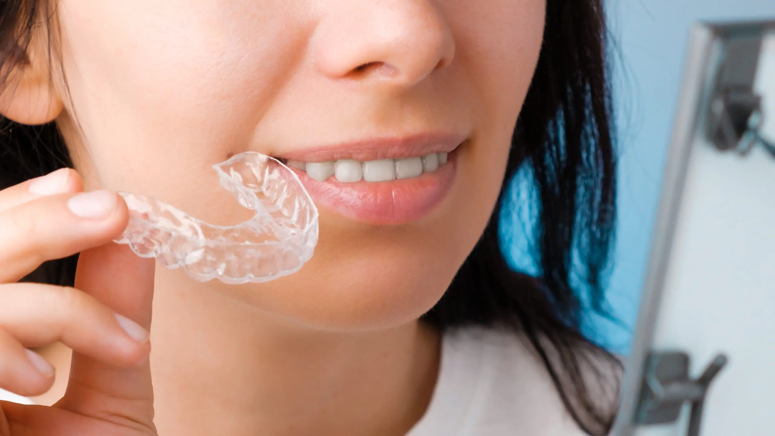 Close up woman holding a transparent removable braces for perfect smile and looking to the mirror. Orthodontic aligners for straightening and whitening teeth