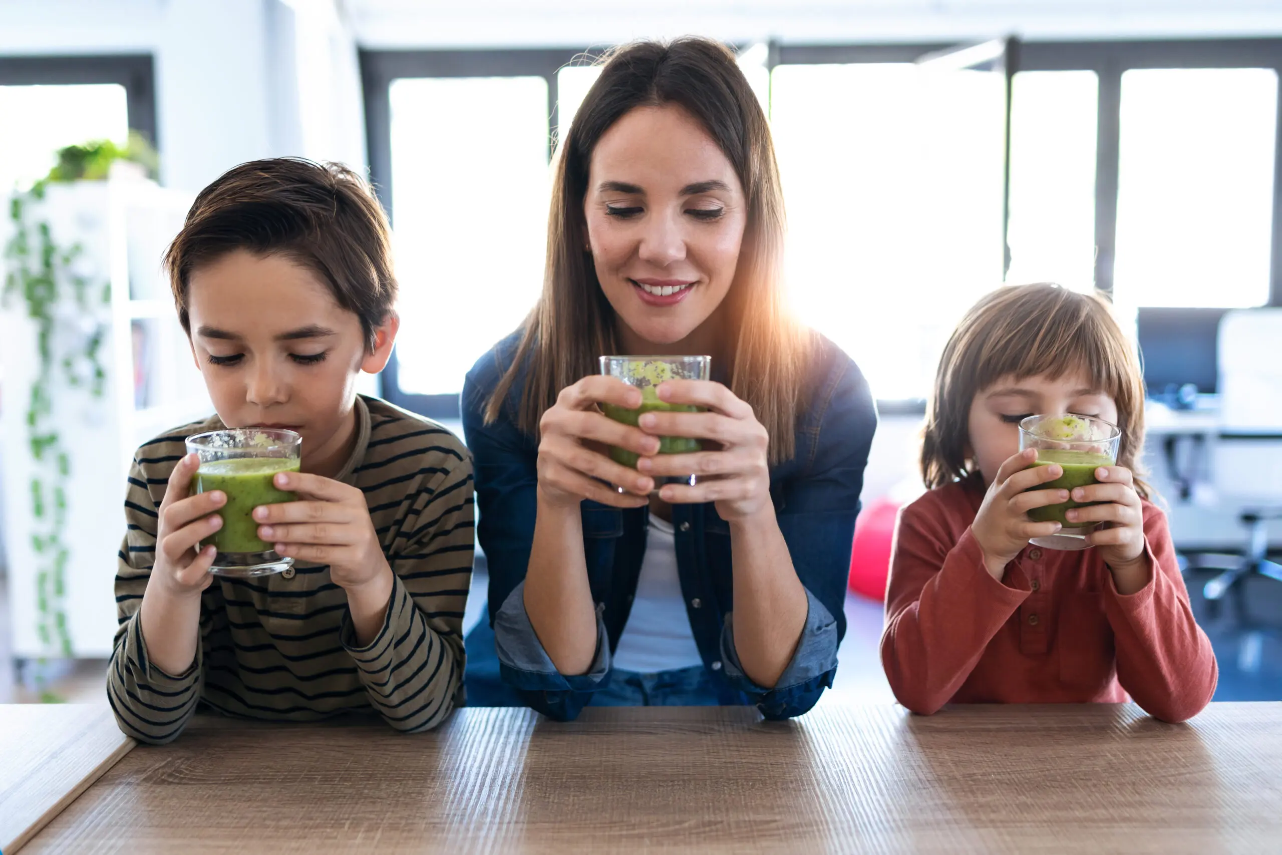 Shot of pretty young mother with her sons drinking detox smoothie in the kitchen at home.