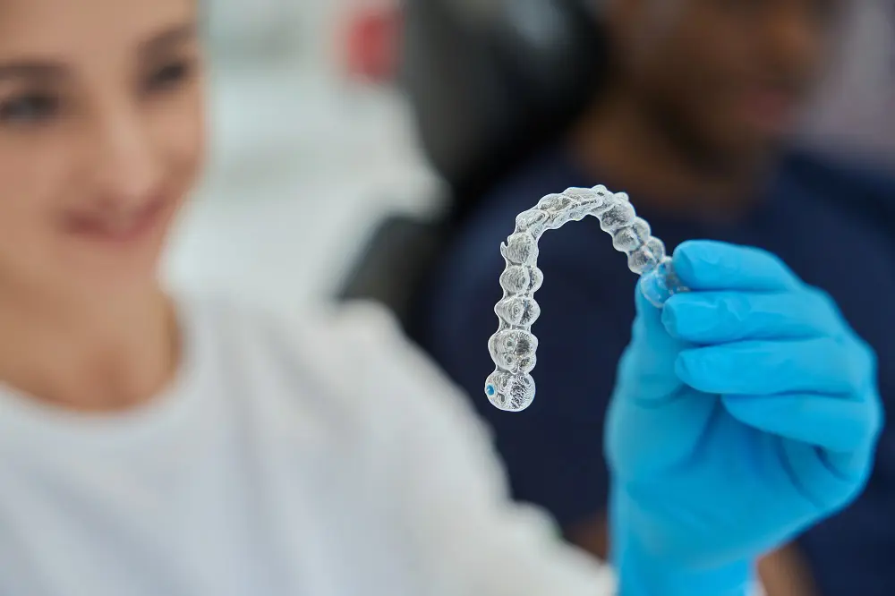 Dental technician holding invisible braces, or clear aligners, removable plastic pieces that fit over patient teeth and can be removed for a couple of hours a day