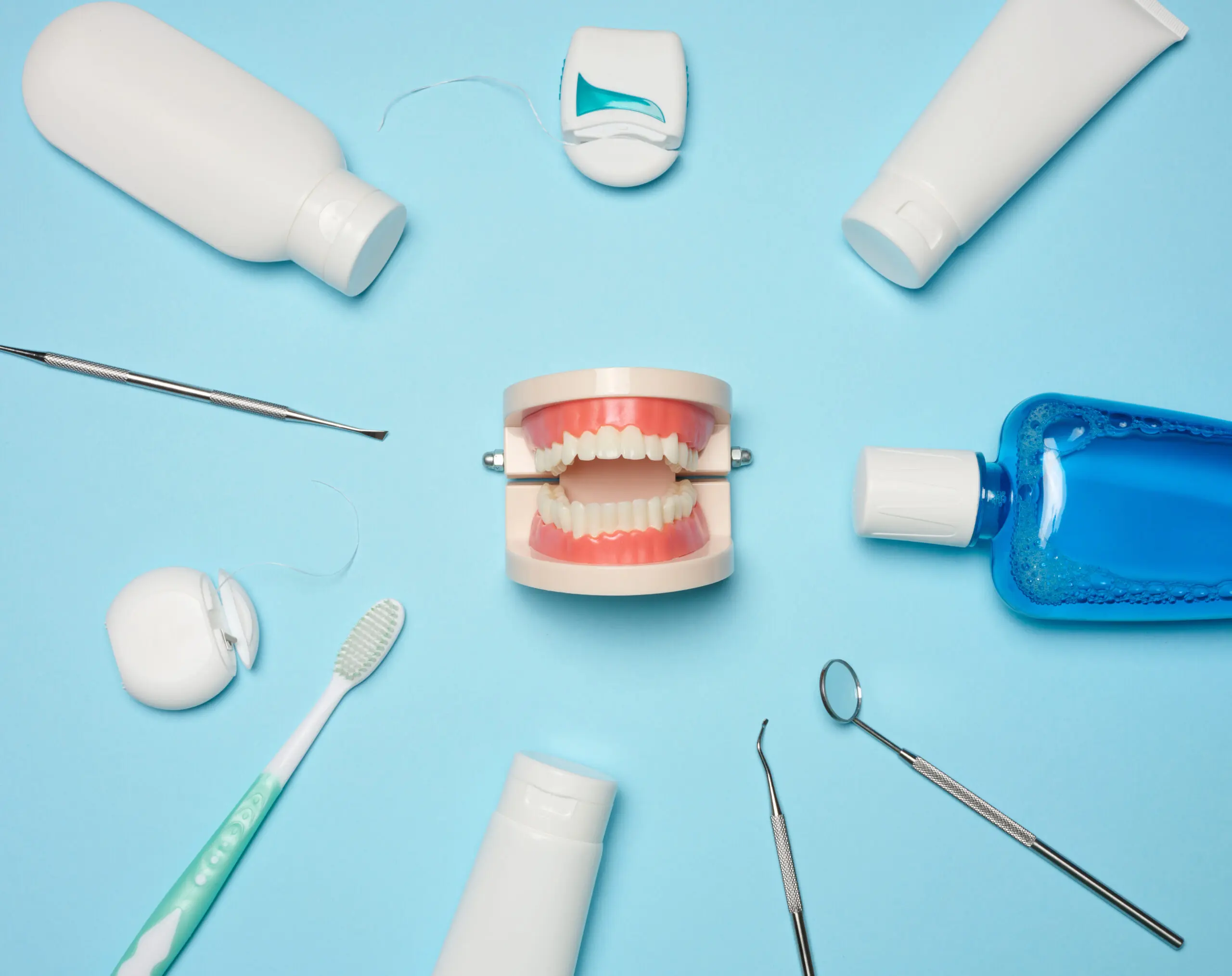 Mouthwash, toothpaste tube, dental floss and medical mirror on a blue background, oral hygiene. Top view