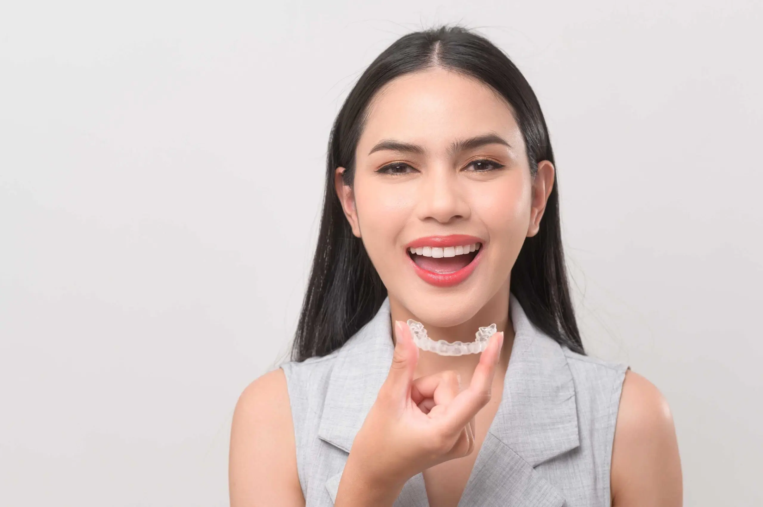 young woman smiling while holding her retainers