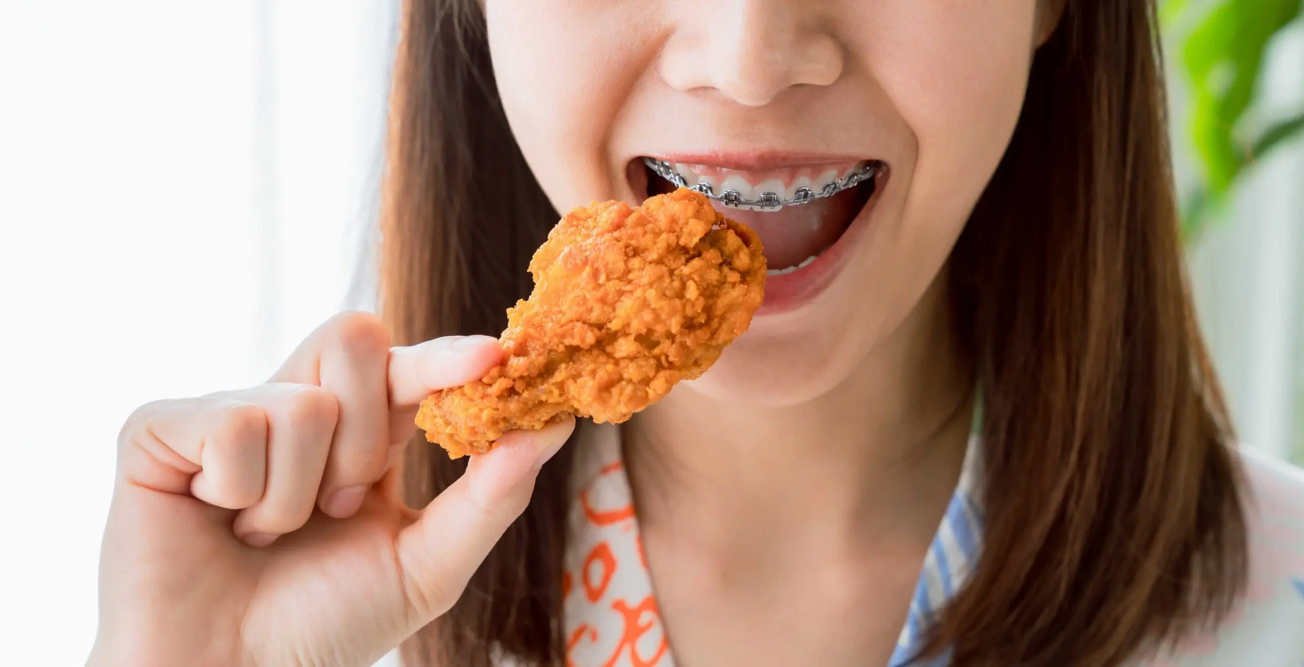 woman with metal braces holding a friend chicken