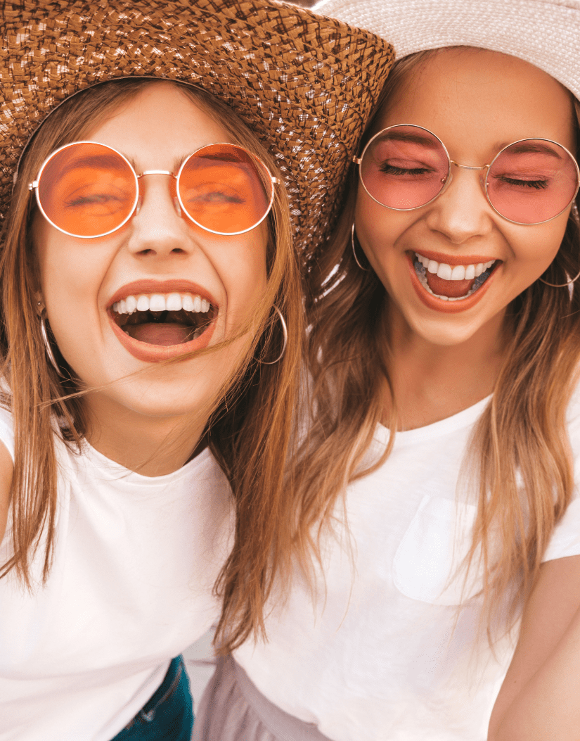 Teen girls in rose colored glasses and hats laughing