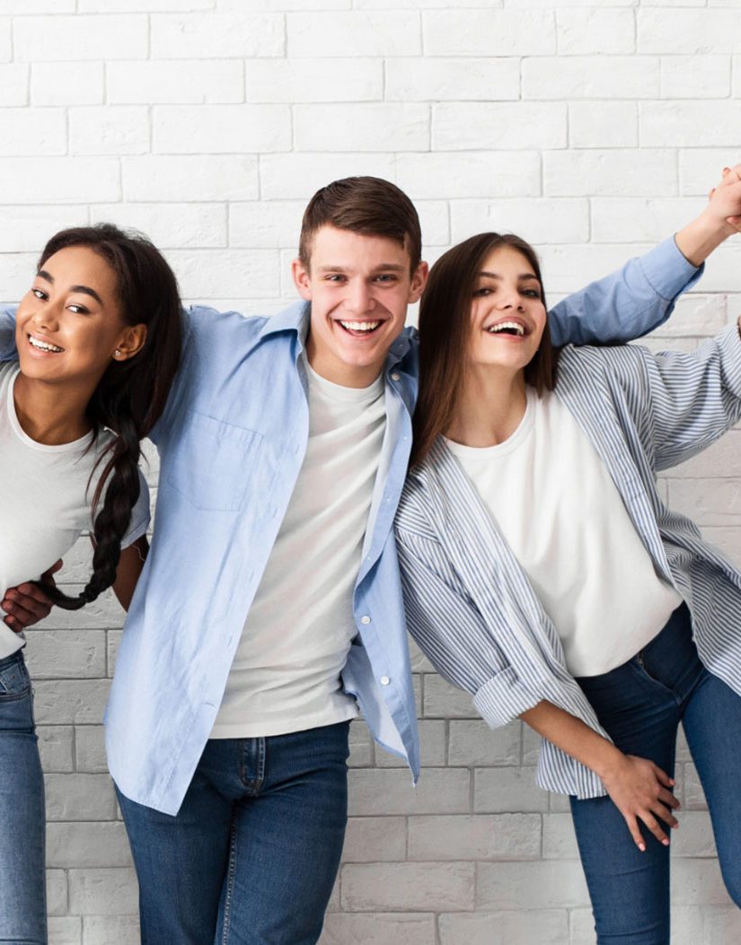 Three teenagers wearing jeans and white tshirts in front of a white washed brick wall.