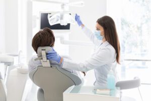 Female dentist doctor greeting patient sitting in dentist chair, turning lamp on, copy space