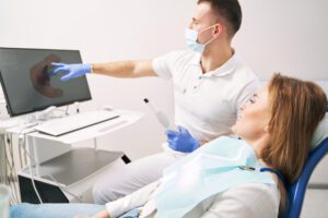 Man stomatologist holding intraoral dental scanner and pointing at computer display while discussing dental treatment with patient