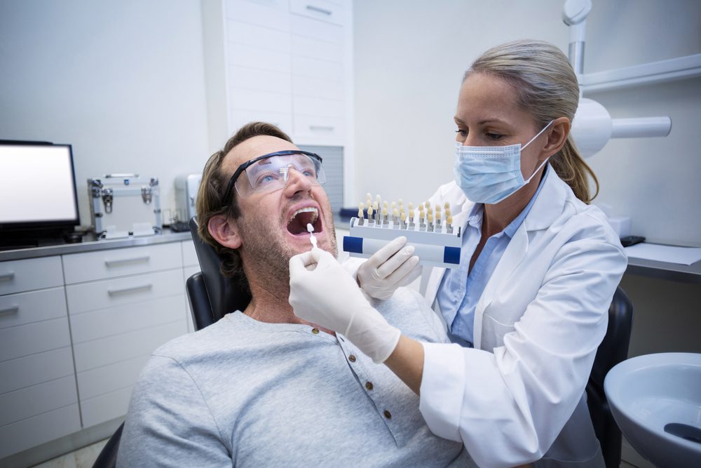 Female dentist examining male patient with teeth shades in dental clinic