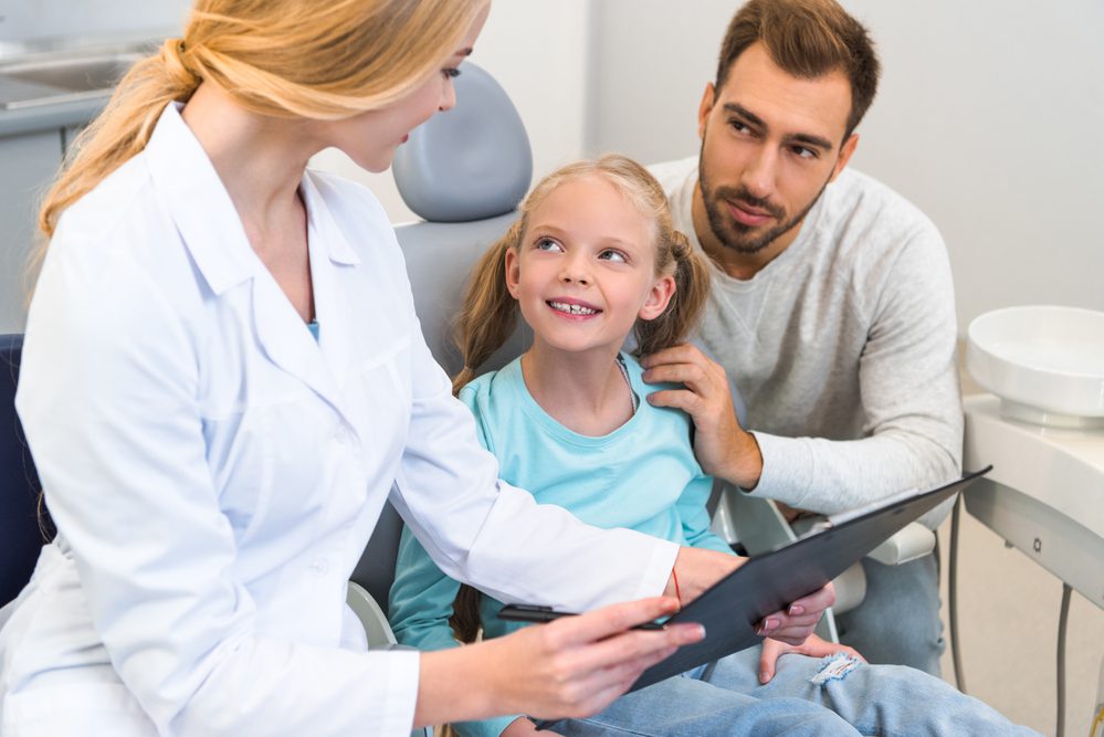 Young female dentist showing clipboard with diagnosis to father