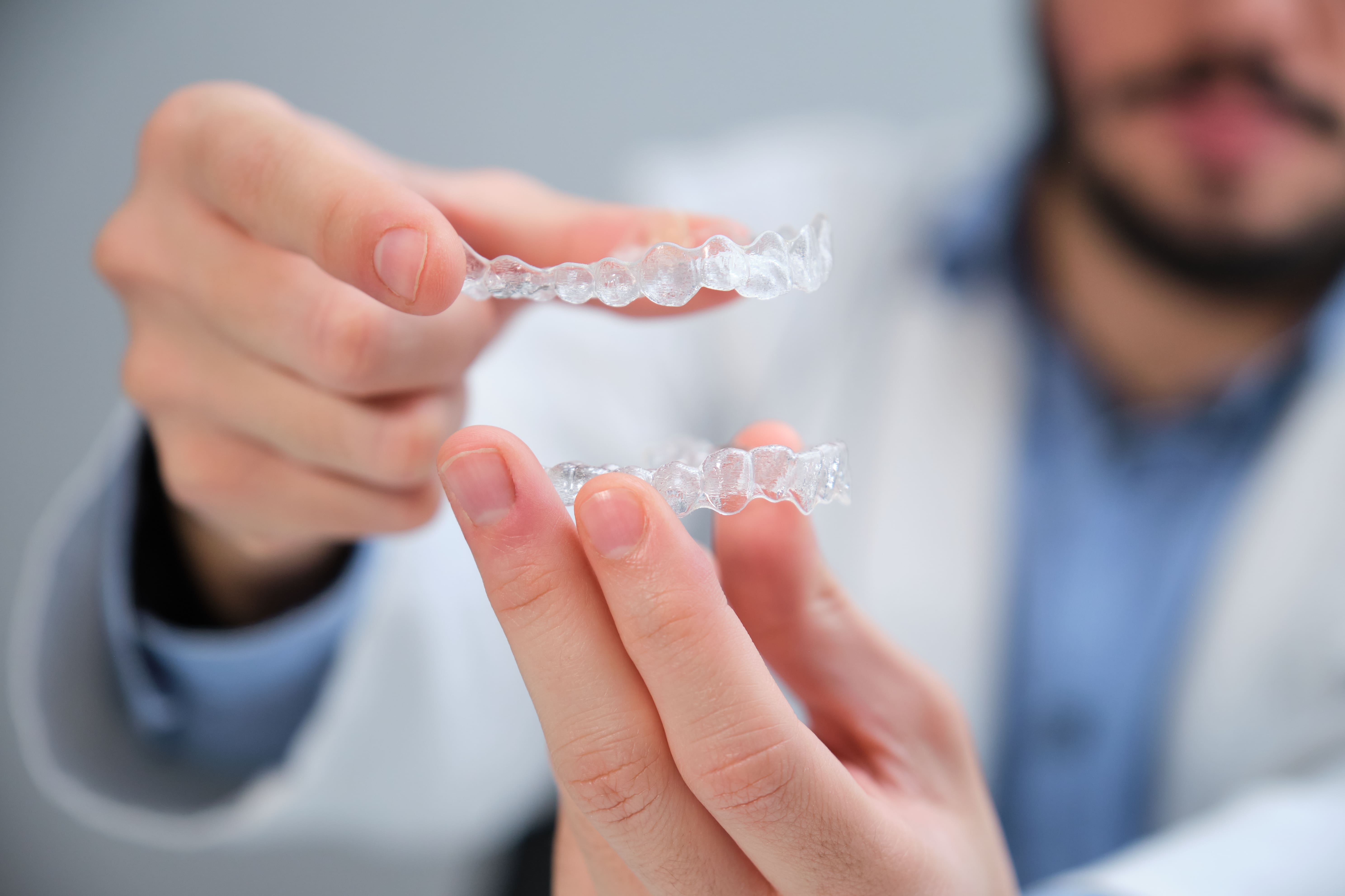 Unrecognizable young orthodontist holding trainer dental braces.