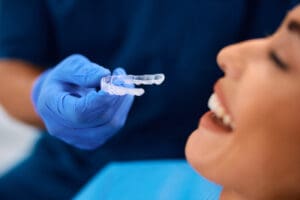 Close up of dentist applying invisible aligners on woman's teeth during appointment at dental clinic.