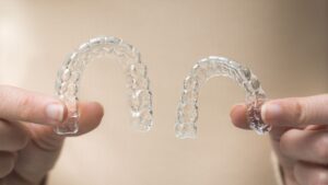 woman's hands holding two side lit transparent retainers on beige background