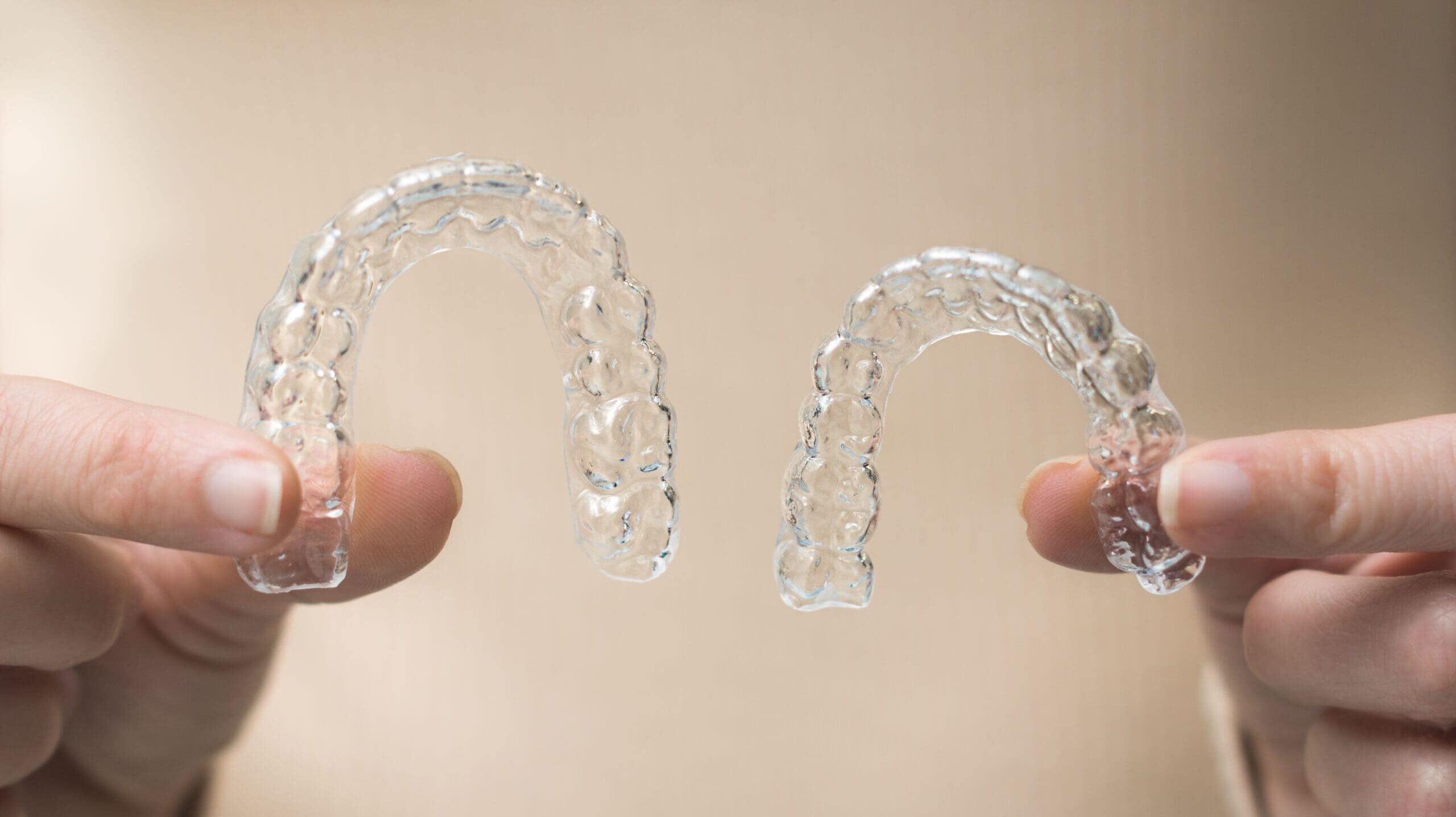 woman's hands holding two side lit transparent retainers on beige background