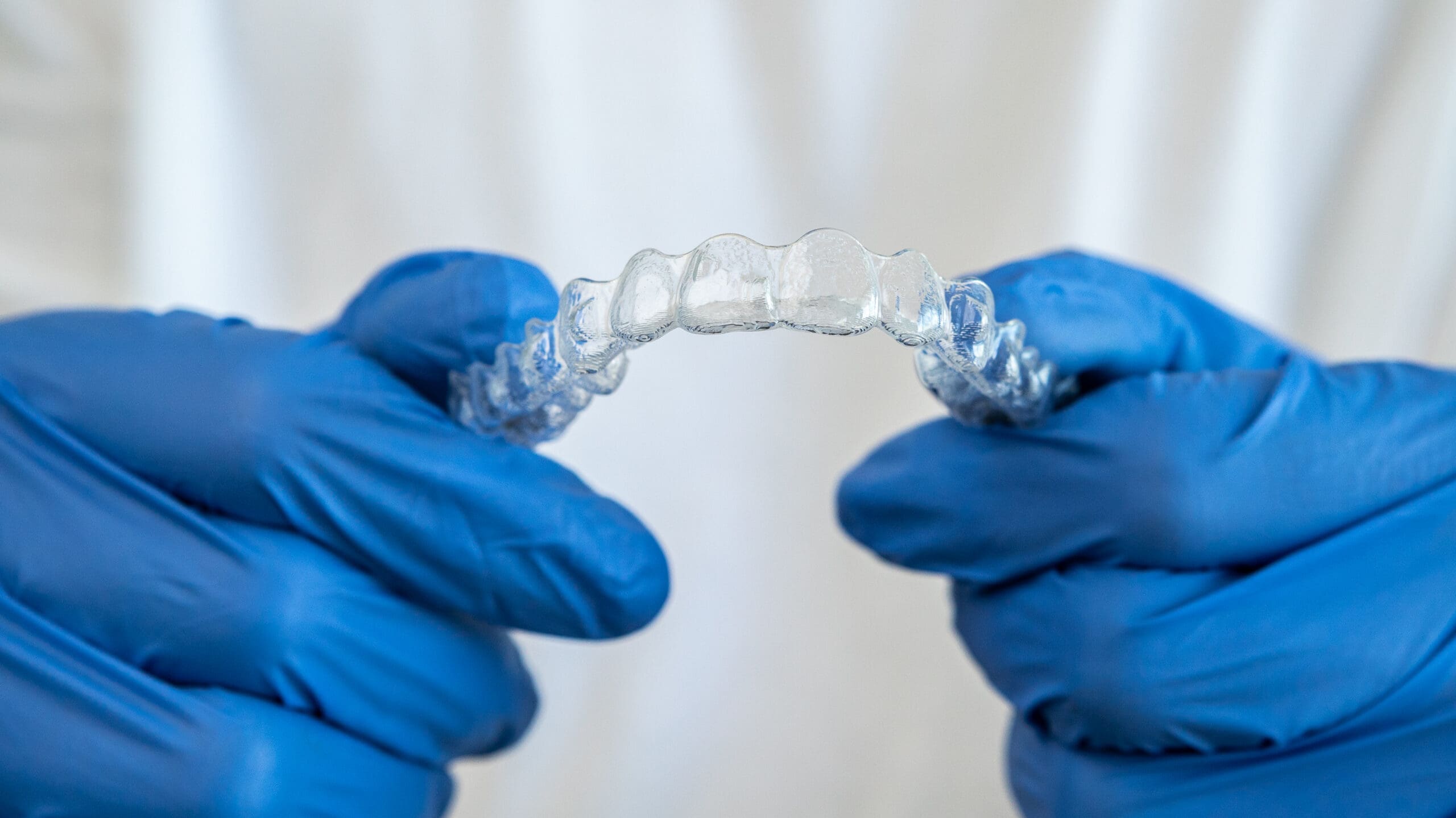 Male hand in gloves holding dental aligner retainer on white background of dental clinic for beautiful teeth treatment. Orthodontic removable straighteners