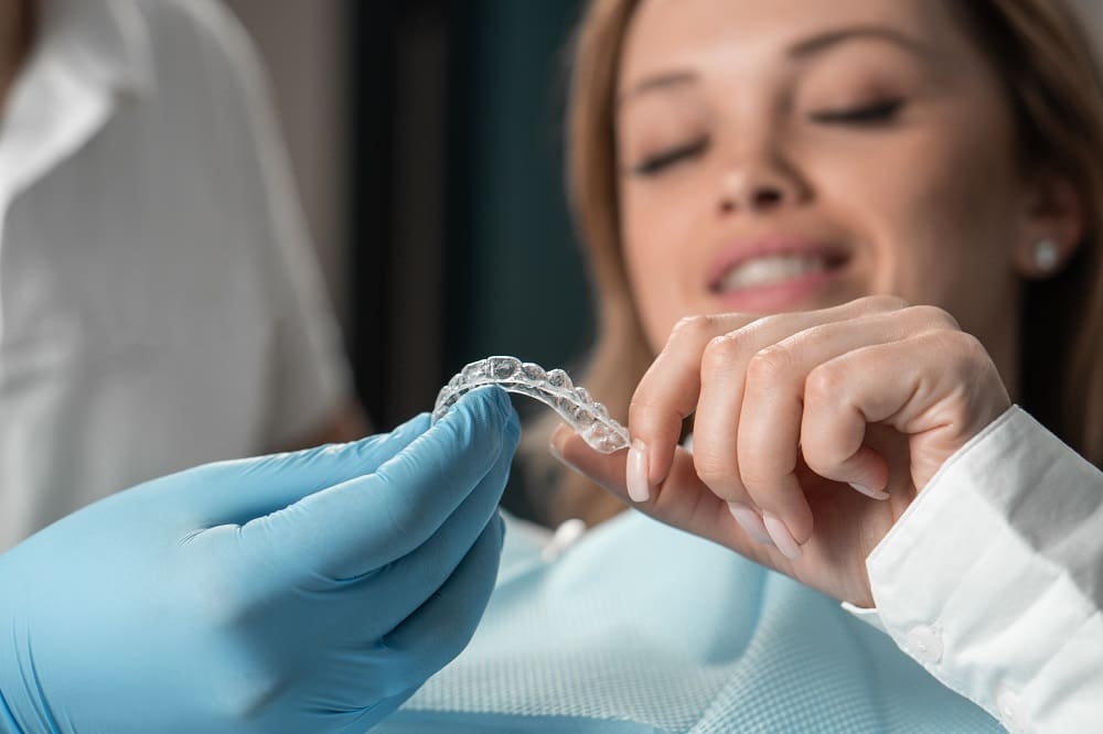 Attentive dentist demonstrating aligner aligner in hands, showing female patient in dental office, preparing for work and striving to make the procedure as comfortable as possible for her patient. High quality photo