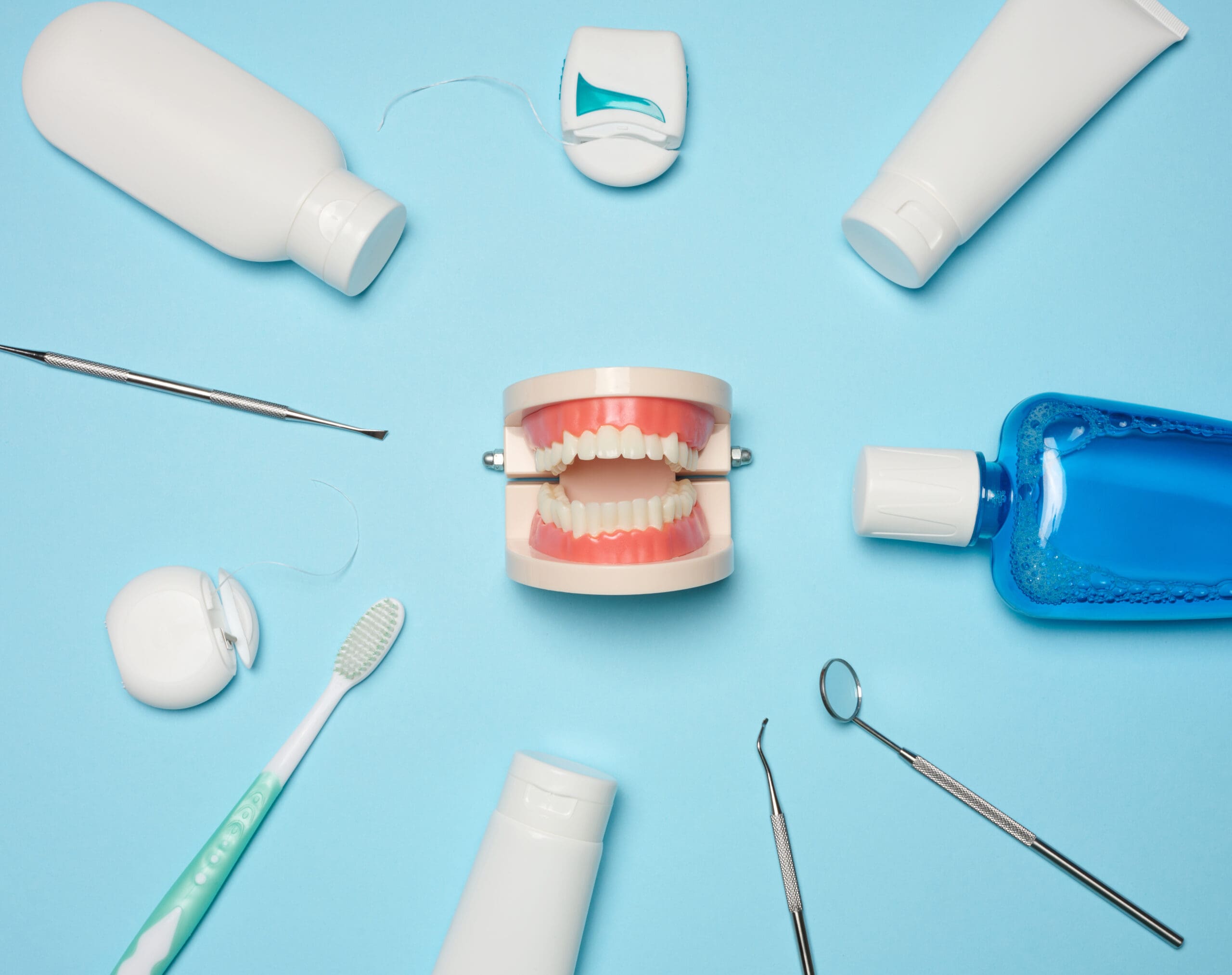 Mouthwash, toothpaste tube, dental floss and medical mirror on a blue background, oral hygiene. Top view
